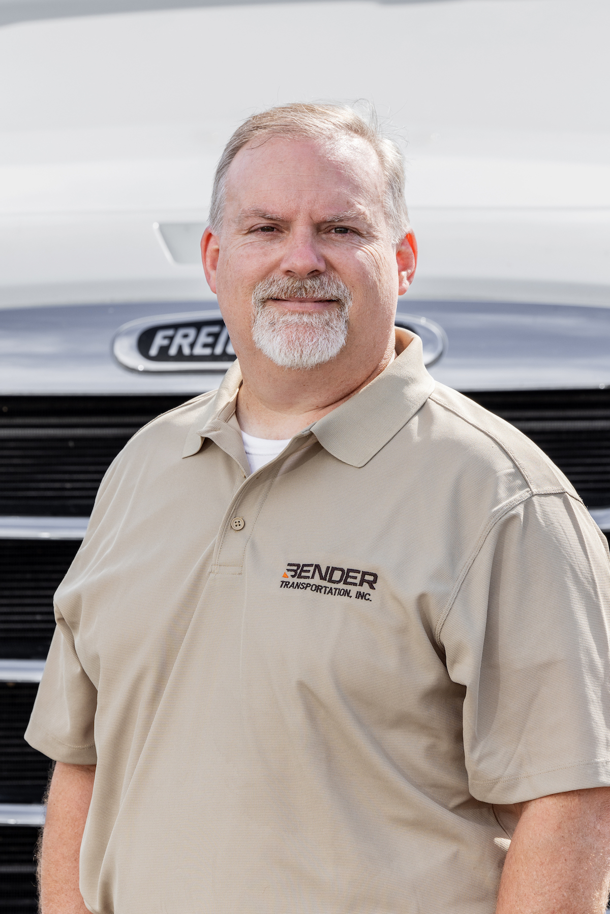 Picture of middle-aged man in a tan shirt posing for a picture in front of a truck.